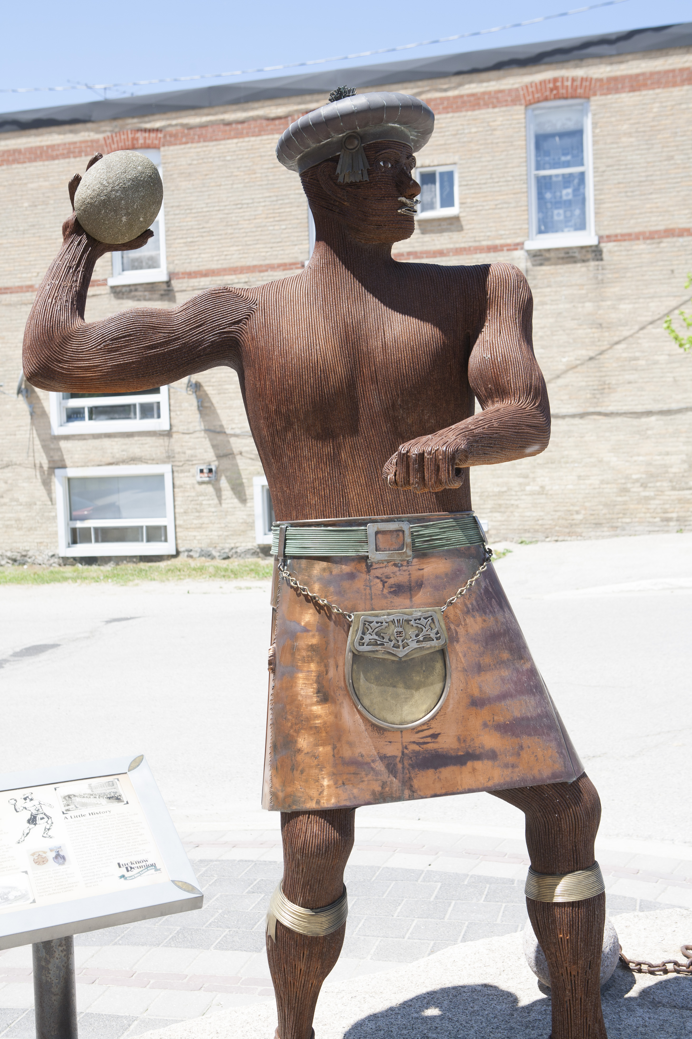 Statue of a strongman, wearing a kilt, throwing a shot put.